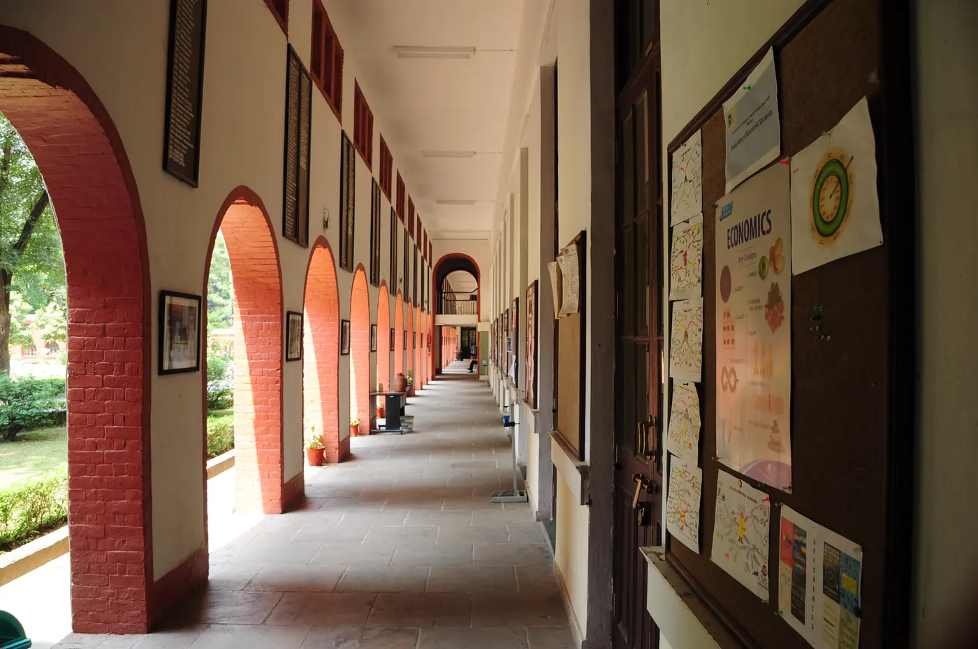 A long open corridor of red-brick arches in the Main Building, notice boards along its inner wall