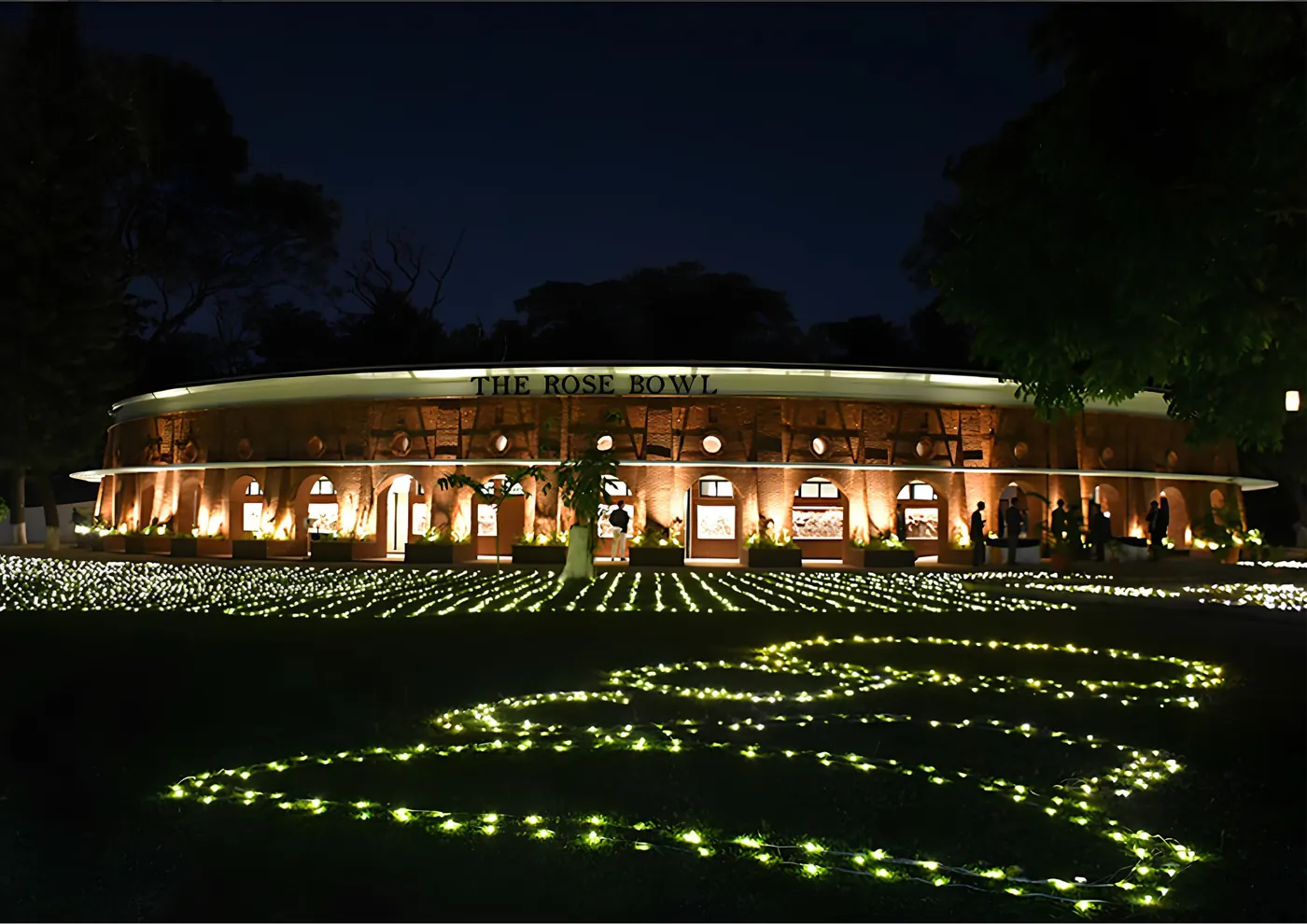 The Rose Bowl at night, its curved front lit and its name along the roof, fairy lights on the lawn spelling DS90